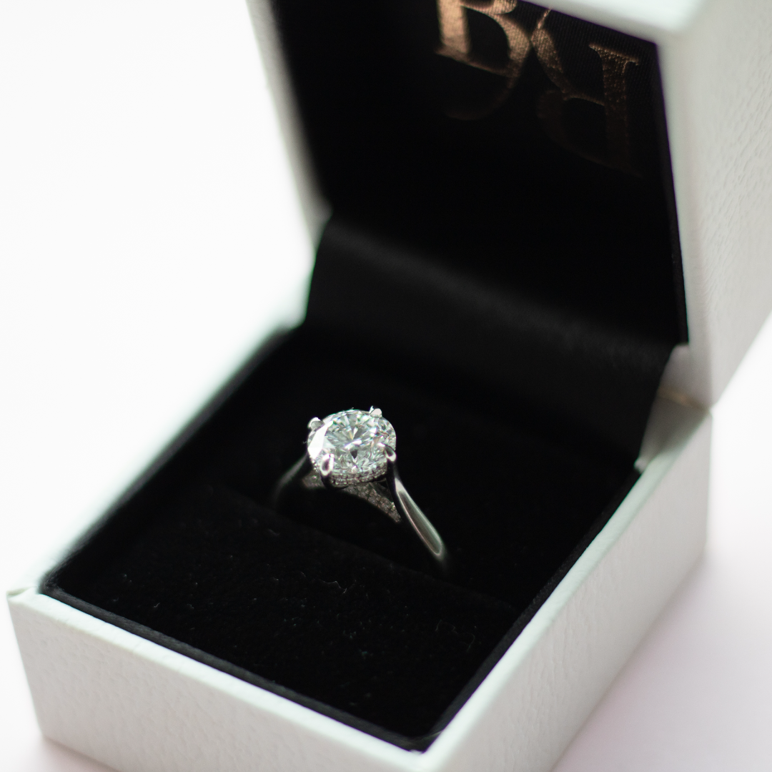 Round brilliant cut diamond with a hidden halo, platinum claws, diamond set bridge and platinum band. Handmade luxury in the UK and Ireland for engagement rings, wedding bands, eternity rings and classic jewellery.