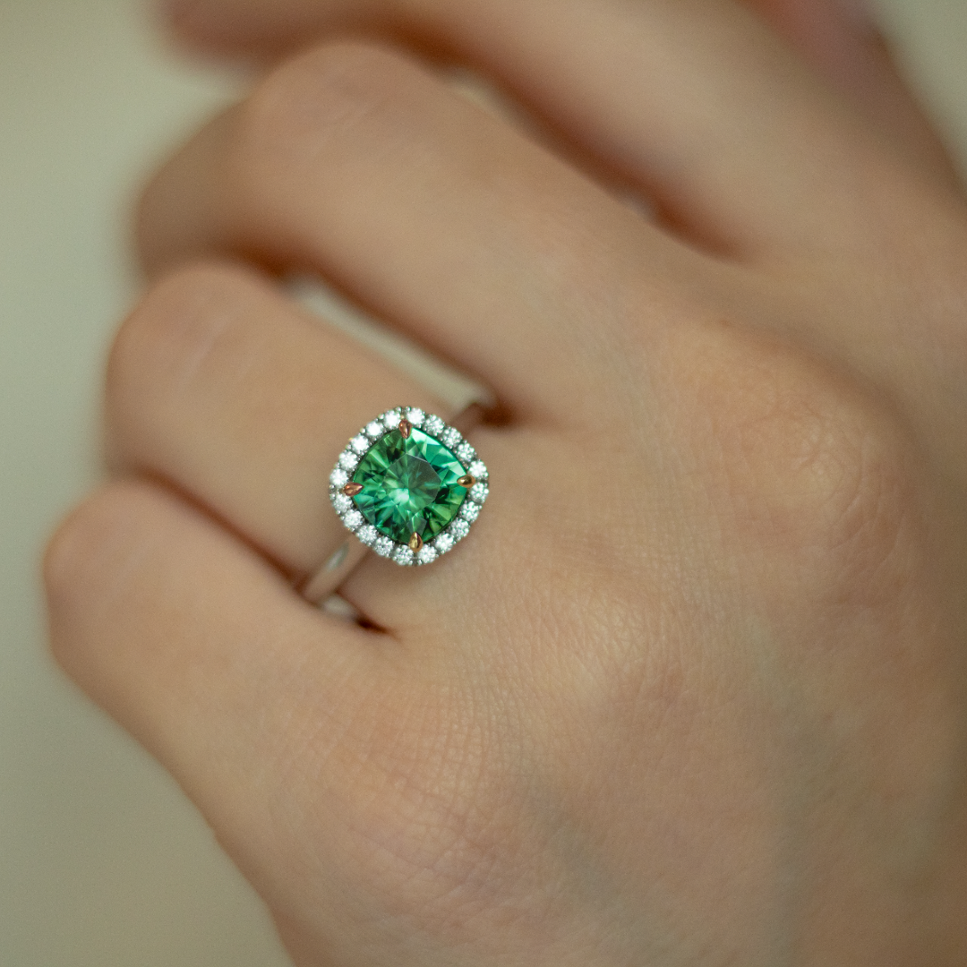 Cushion cut green tourmaline set with 18ct yellow gold claws and a diamond halo in platinum. Handmade luxury in the UK and Ireland for engagement rings, wedding bands, eternity rings and classic jewellery.