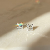 Asscher-cut diamond earrings on a marble surface with a warm light background. Irish dublin based jewellers, Natural and Lab diamonds. Set in platinum.