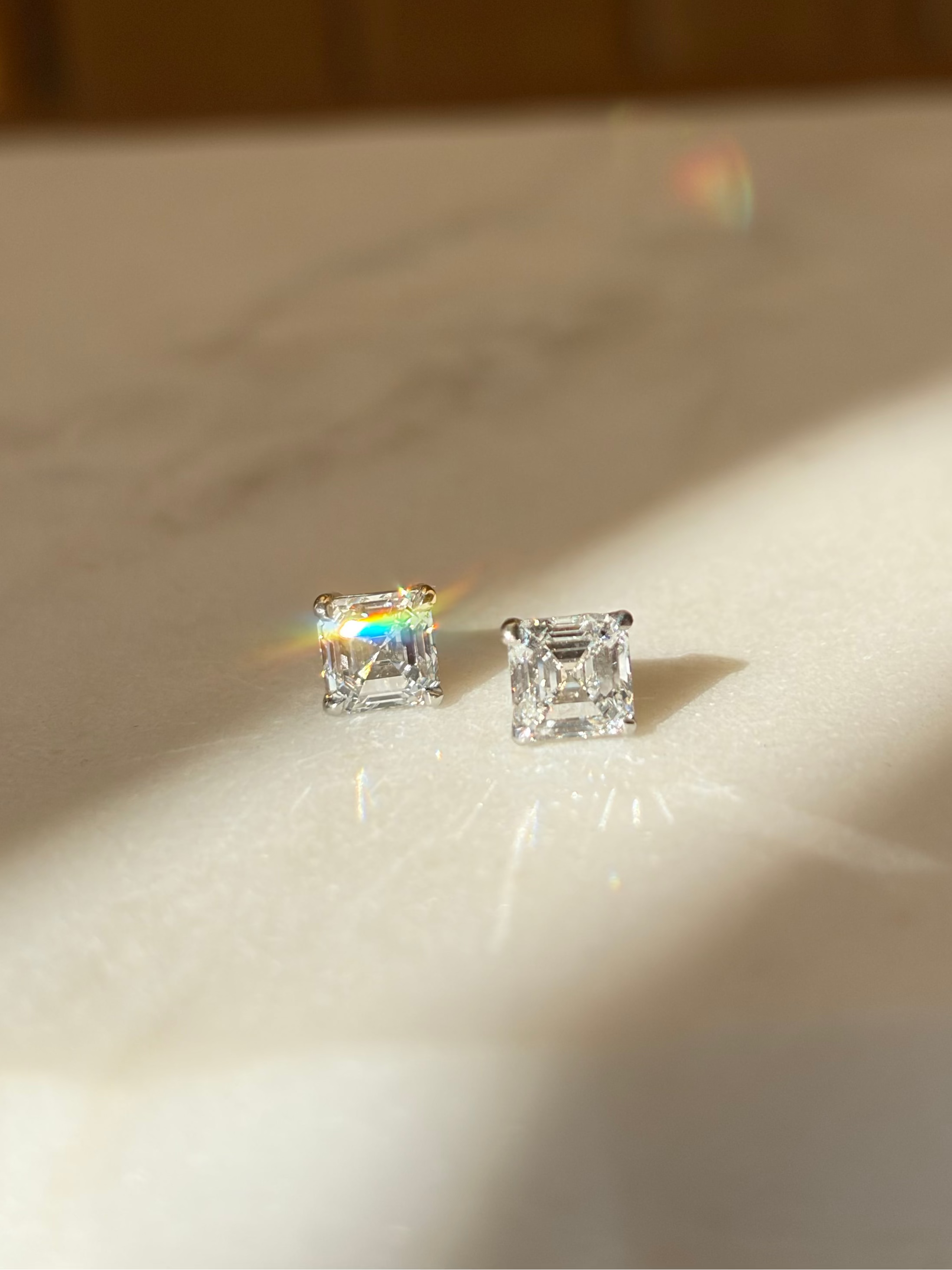 Asscher-cut diamond earrings on a marble surface with a warm light background. Irish dublin based jewellers, Natural and Lab diamonds. Set in platinum.