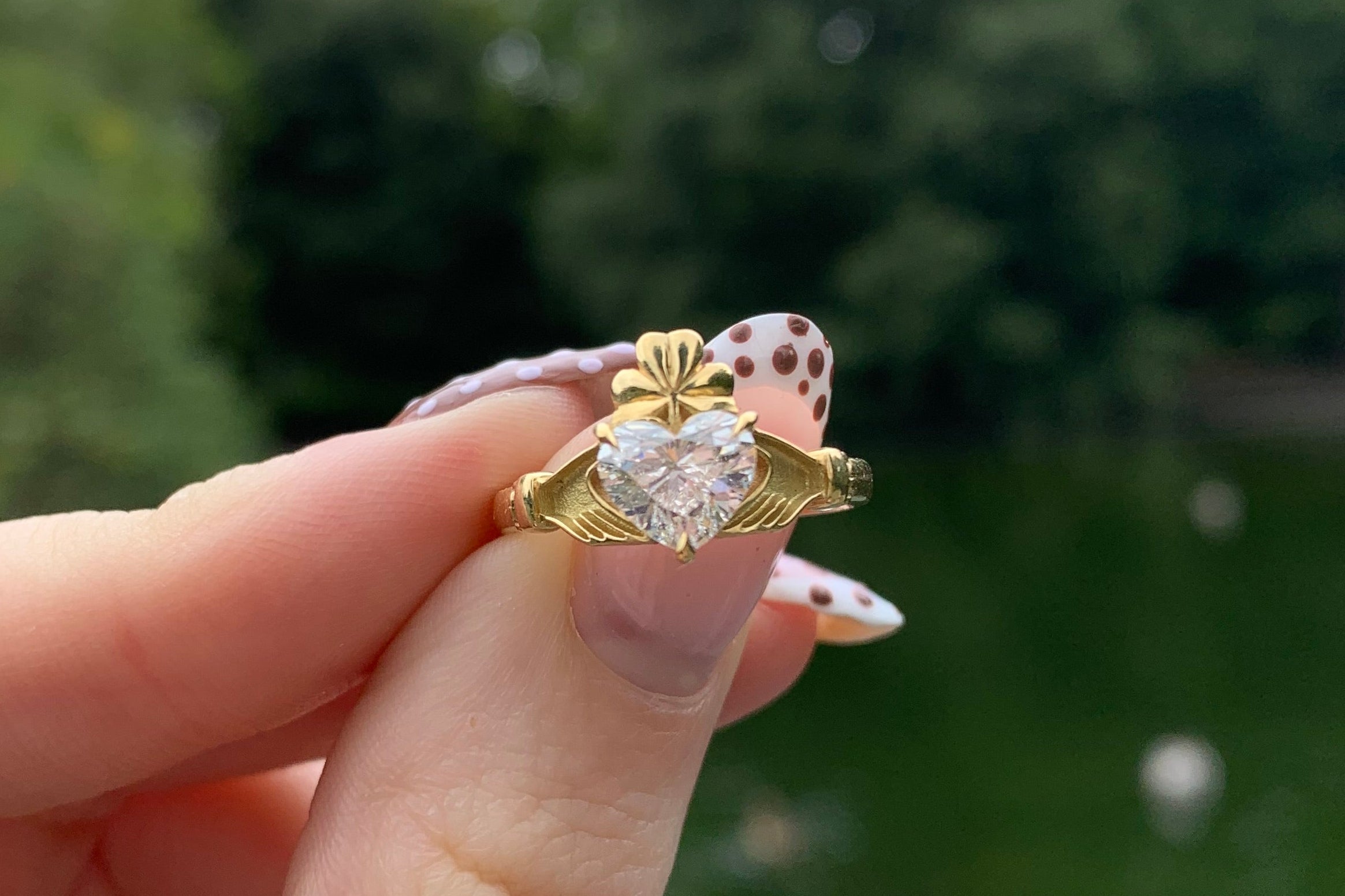 gold claddagh ring with diamond heart and shamrock crown. Helf in front of Stephens green lake.