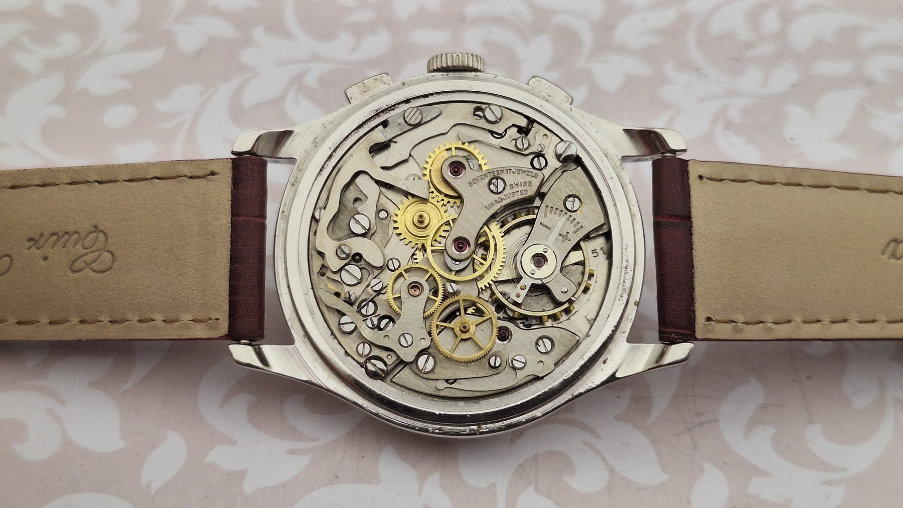 Vintage watch with visible mechanical components on a patterned background