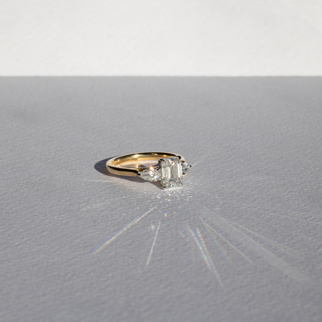 Emerald cut diamond with pear cut diamond shoulders and platinum claws and an 18ct yellow gold band. Handmade luxury in the UK and Ireland for engagement rings, wedding bands, eternity rings and classic jewellery.