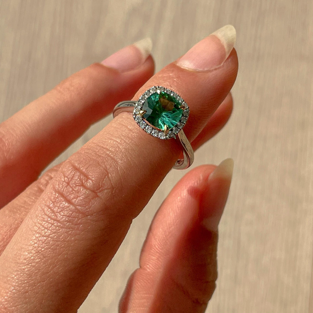 Cushion cut green tourmaline set with 18ct yellow gold claws and a diamond halo in platinum. Handmade luxury in the UK and Ireland for engagement rings, wedding bands, eternity rings and classic jewellery.