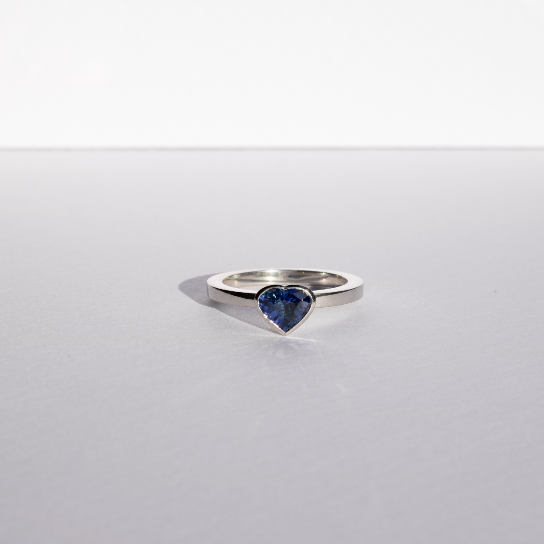 Heart shaped blue sapphire bezel set  with a hidden diamond halo in platinum. Handmade luxury in the UK and Ireland for engagement rings, wedding bands, eternity rings and classic jewellery.