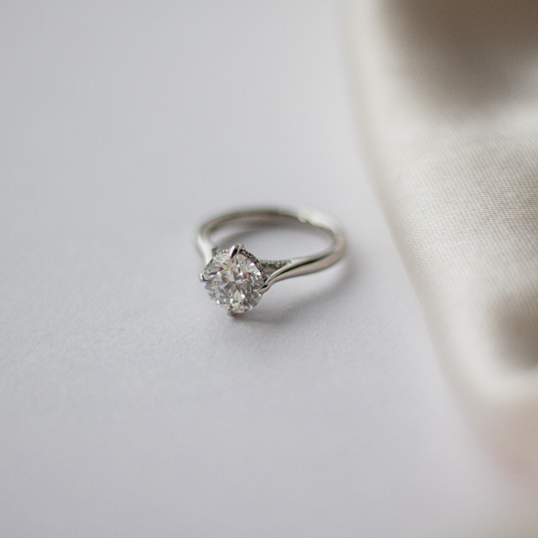 Round brilliant cut diamond with a hidden halo, platinum claws, diamond set bridge and platinum band. Handmade luxury in the UK and Ireland for engagement rings, wedding bands, eternity rings and classic jewellery.