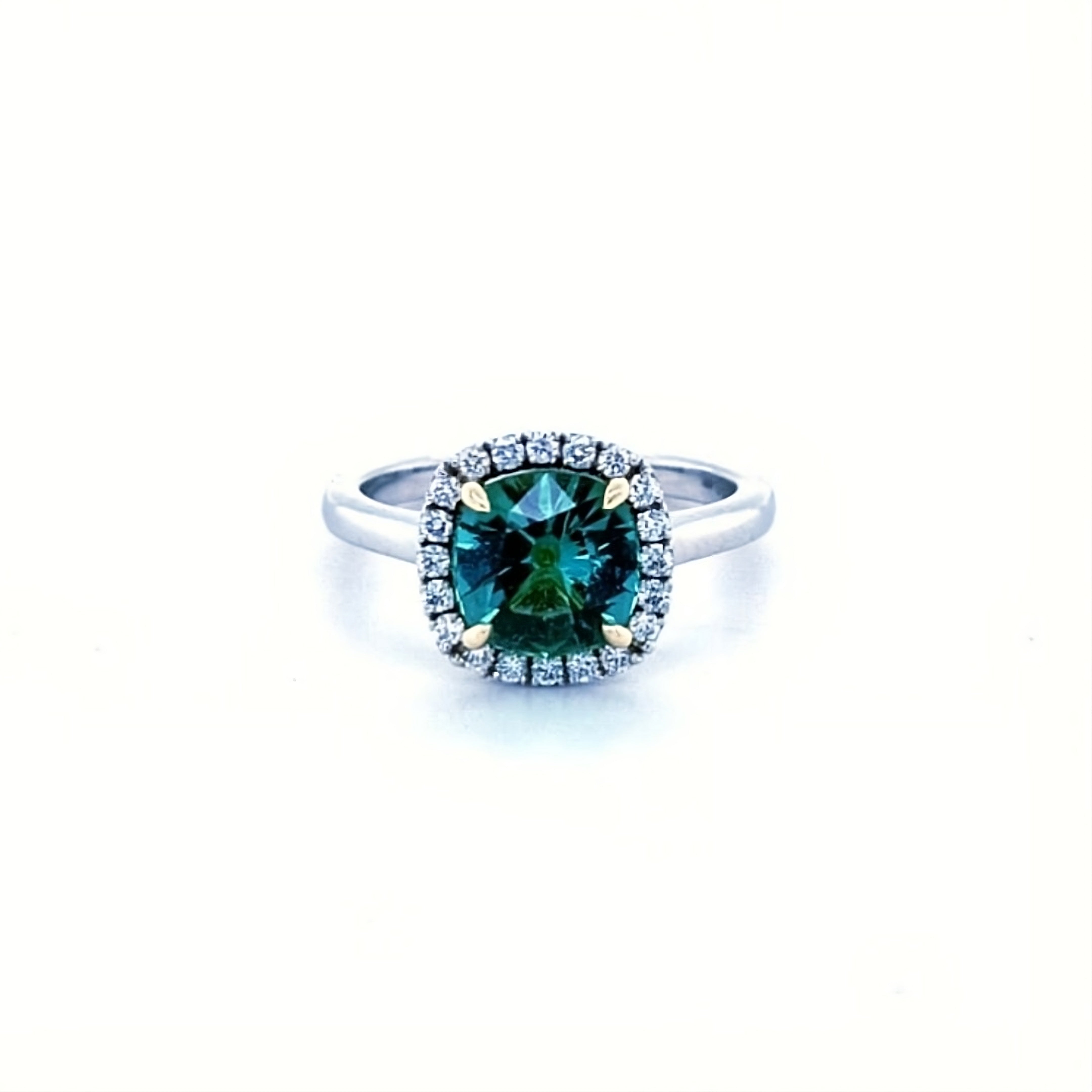 Cushion cut green tourmaline set with 18ct yellow gold claws and a diamond halo in platinum. Handmade luxury in the UK and Ireland for engagement rings, wedding bands, eternity rings and classic jewellery.
