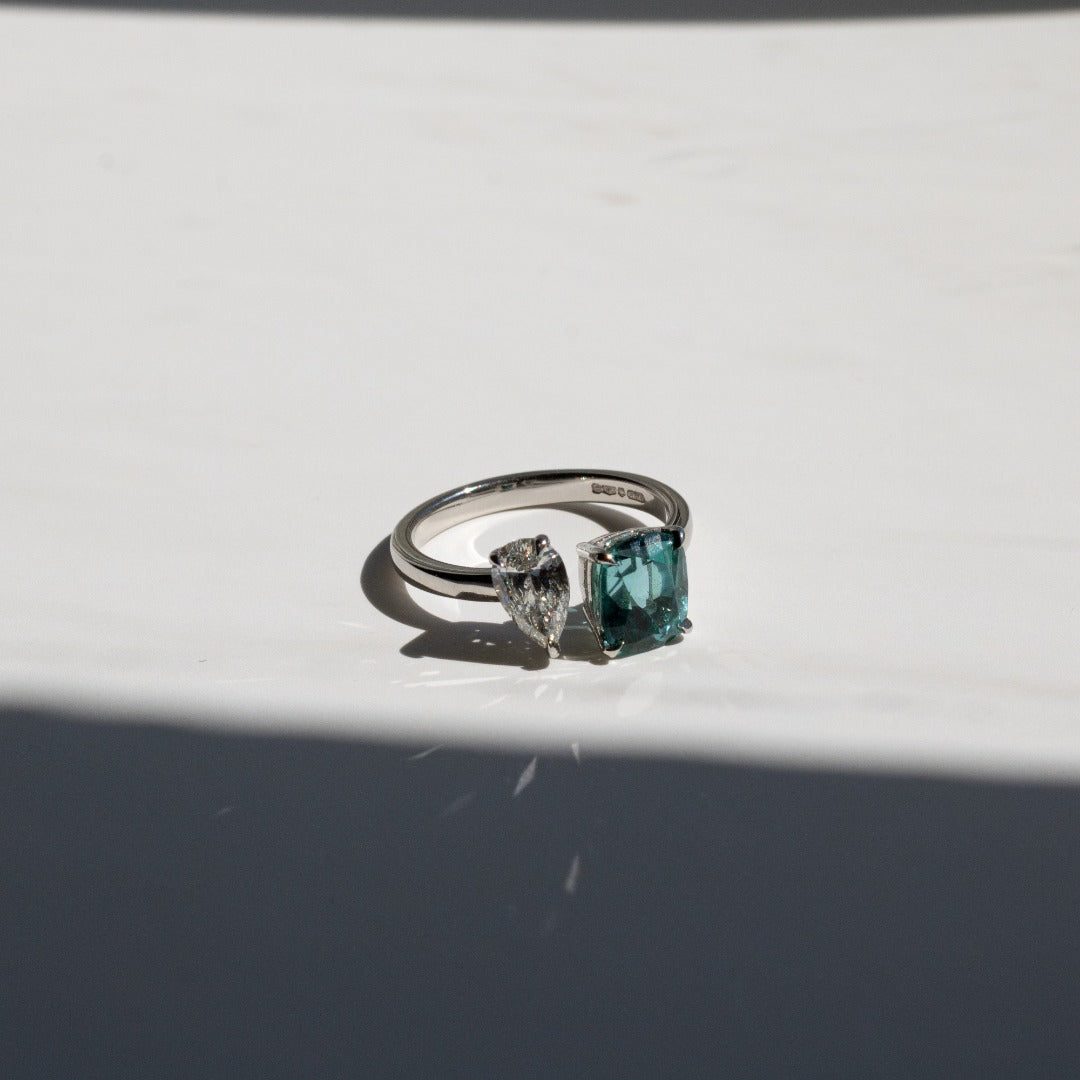Toi et Moi with a green cushion cut tourmaline and pear cut diamond with platinum claws on a platinum band. Handmade luxury in the UK and Ireland for engagement rings, wedding bands, eternity rings and classic jewellery.