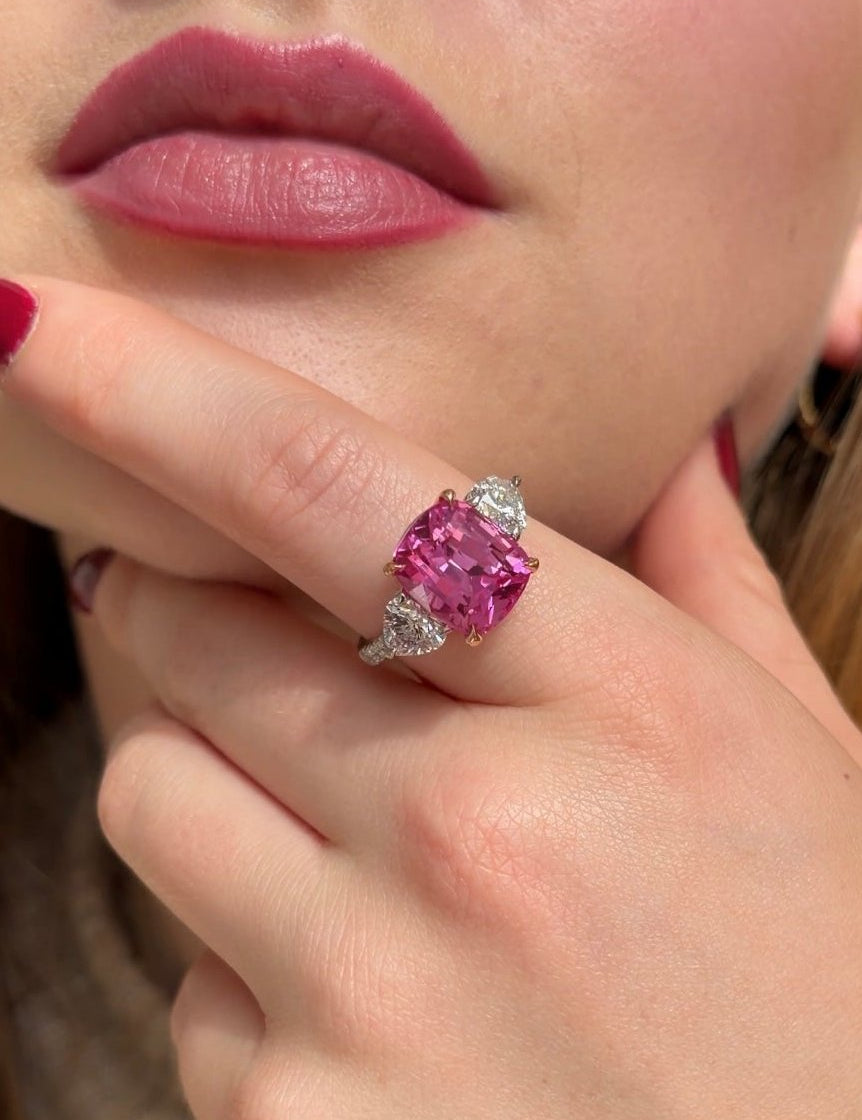 Cushion pink sapphire with rose gold claws, diamond heart shoulders and diamond band set in platinum. Three stone sapphire gemstone ring.
