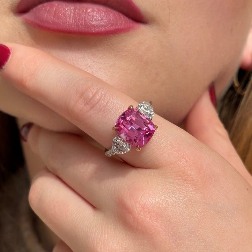 Cushion pink sapphire with rose gold claws, diamond heart shoulders and diamond band set in platinum. Three stone sapphire gemstone ring.